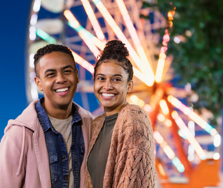Young black man and woman standing in front of a brightly coloured Ferris wheel at night